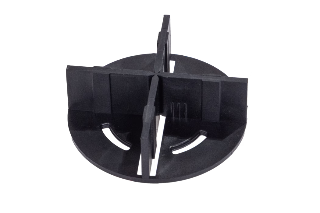 codex_Dummy_BL Cross_2024-04 This image shows a black plastic spacer designed for tile installations. It features a circular base with a cross-like configuration that includes two pairs of vertical panels protruding from the center. The panels are designed to ensure even spacing between tiles while they are being laid. The base has circular holes that can help in securing or aligning the spacer during use. This tool is essential for achieving uniform joint widths in tiling projects.